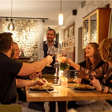 A cheerful group of four people is celebrating in a restaurant and clinking wine glasses. In the background, an attentive waiter can be seen, making for a pleasant evening for the guests.