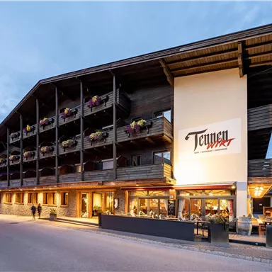 Ein modernes Hotelgebäude mit einem traditionellen Holzdesign. Es gibt Balkone mit Blumen und eine einladende Atmosphäre.