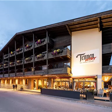 A modern hotel building with a traditional wooden design. There are balconies with flowers and an inviting atmosphere.
