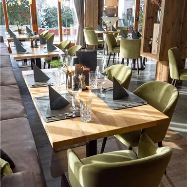 Ein modernes Restaurant mit hellen Tischen und stilvollen, grünen Stühlen. Die Tische sind elegant eingedeckt und bieten eine einladende Atmosphäre.