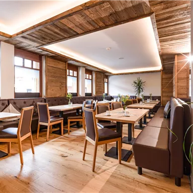 A cozy restaurant with wood decor and large windows. The tables are neatly set, and plants create an inviting atmosphere.