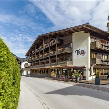 Ein charmantes Hotel mit Holzbalconys und einer schönen Fassade. Die Straße führt direkt zum Eingang, umgeben von grünen Bäumen.
