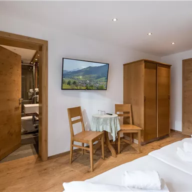 Ein modernes Zimmer mit Holzfußboden und gemütlicher Einrichtung. Ein Tisch mit zwei Stühlen und ein schöner Blick auf die Berge durch ein Bild an der Wand.