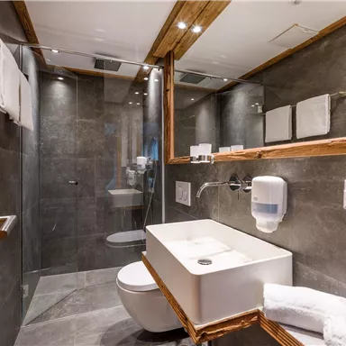 Ein modernes Badezimmer mit eleganten grauen Fliesen und Holzdetails. Es verfügt über eine Dusche, ein Waschbecken und gepflegte Handtücher.