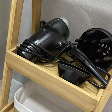 A wooden shelf with a black hair dryer and a bowl. Below the shelf is a basket.