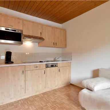 Eine moderne Küchenzeile mit Holzschränken und einem Herd. Daneben befindet sich ein gemütliches Sofa in einem hellen Raum.