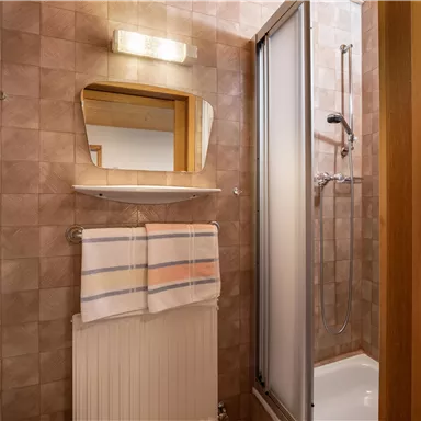 A bathroom with a shower, a mirror, and a towel rack. The walls are decorated with square tiles in neutral colors.