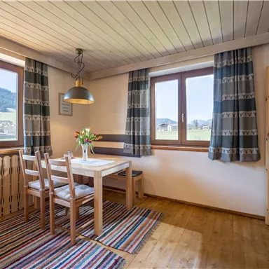A cozy dining area with a wooden table and chairs. Large windows provide a view of the landscape.