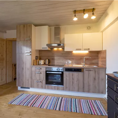 A modern kitchen with wooden cabinets and a stove. The floor is covered with a colorful carpet.