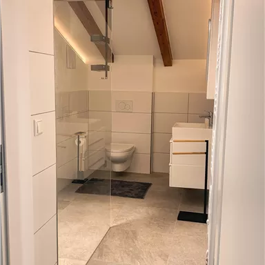 A modern bathroom with bright tiles and wooden beams. In the background, a shower and a washbasin can be seen.
