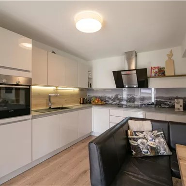 Modern kitchen with white cabinets and an elegant countertop. A cozy living area with a black sofa and a dining table is also visible.