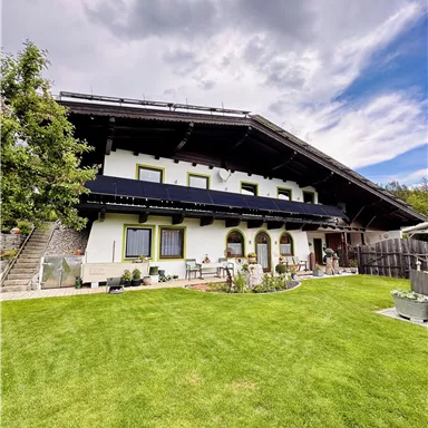 A traditional house with a large garden and many plants. The sky is cloudy and there is a hint of blue sky.
