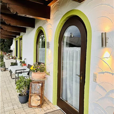 A beautiful entrance with a brown gate and green accents.
Plants and tables stand in front of the door, creating an inviting atmosphere.