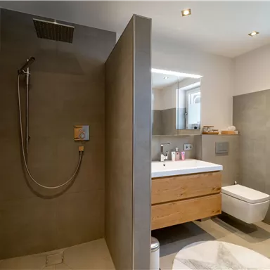 A modern bathroom with a shower and a wooden sink. The walls are in neutral gray tones and the lighting is pleasant.