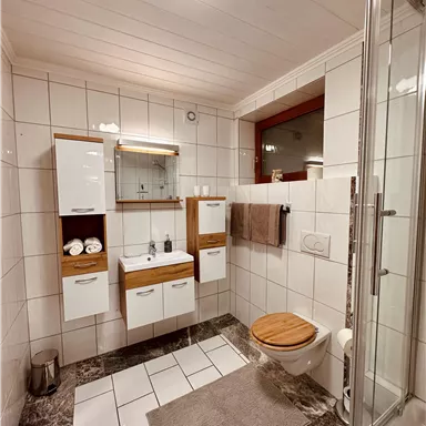 A modern bathroom with bright tiles and wooden accents. The shower is separated by a glass door, and the space feels clean and inviting.