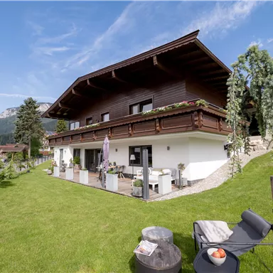 A modern house in alpine style with a large garden. The clear sky and the surrounding landscape provide a relaxed atmosphere.