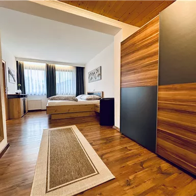 A modern room with two beds and a large mirror. The wooden floors and windows create a pleasant atmosphere.