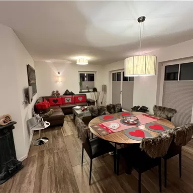 Ein modernes Wohnzimmer mit einem runden Tisch und Stühlen. Der Tisch ist dekoriert mit roten Herzen, während die Wände hell und einladend sind.