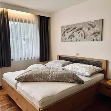 A cozy bedroom with a large double bed and two pillows. Soft colors and a large window create a bright atmosphere.