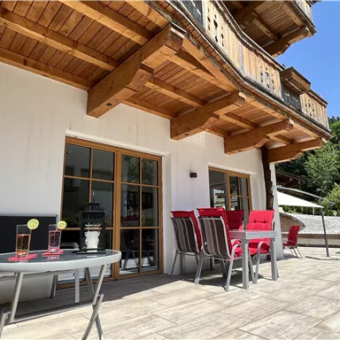 Eine gemütliche Terrasse mit modernen Möbeln und Blick ins Grüne. Auf dem Tisch stehen Getränke bereit, ideal für entspannte Stunden im Freien.
