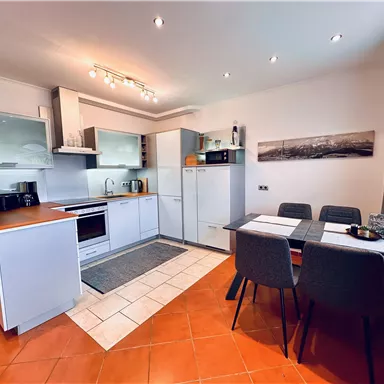 Modern kitchen with bright furniture and a dining table. The space is well-lit and has an inviting atmosphere.