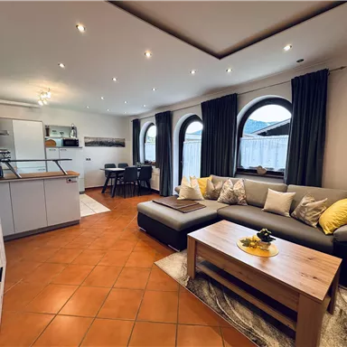 A modern living room with a cozy couch and a wooden table. The large windows provide plenty of daylight and an inviting atmosphere.