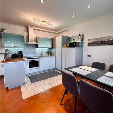 A modern kitchen with white cabinets and an elegant dining table. The space is bright and friendly designed.