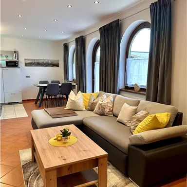 A cozy living room with a comfortable sofa and a wooden table. Large windows provide plenty of light and an inviting atmosphere.