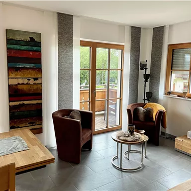 Ein modernes Wohnzimmer mit zwei gemütlichen Sesseln und einem Tisch. Große Fenster lassen viel Licht herein und bieten einen Blick auf den Außenbereich.
