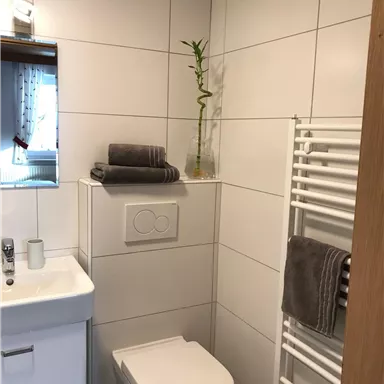 A modern bathroom with bright tiled walls. It features a sink, a toilet, and towels on a towel rack.