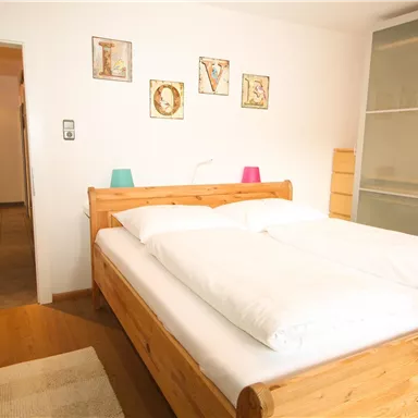 Ein gemütliches Schlafzimmer mit einem großen Holzbett und weißen Bettdecken. Die Wände sind mit dekorativen Bildern geschmückt, und es gibt einen hellen, einladenden Charakter.