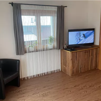 A cozy living space with a television and a black chair. Natural light is visible through the window.