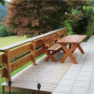 A cozy terrace area with a wooden table and benches. In the background, green fields and trees can be seen.