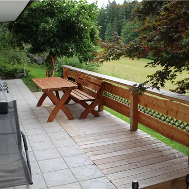 A cozy terrace with a wooden table and chairs.
Surrounded by green trees and a vast field.