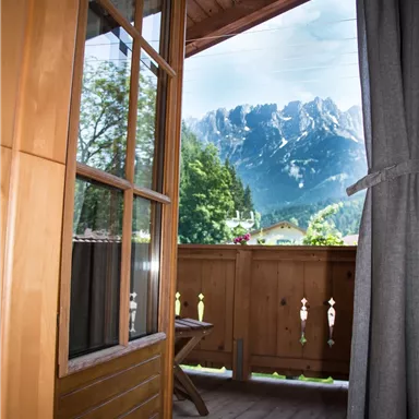 A view from a balcony of majestic mountains. The room is surrounded by warm wood and has a cozy charm.