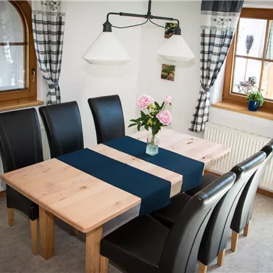 A cozy dining area with a wooden dining table and black chairs. A vase of roses is on the table.