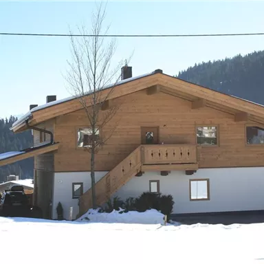 A cozy chalet in winter, surrounded by snow and mountains. The wooden architecture gives the house a rustic charm.