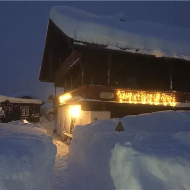 A wintry chalet at twilight, surrounded by deep snow. Lights give the building a cozy atmosphere.