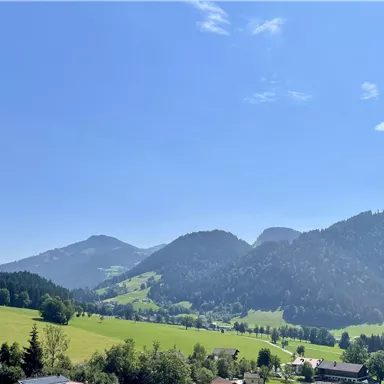 Eine malerische Landschaft mit sanften Hügeln und majestätischen Bergen. Der Himmel ist klar und blau, ideal für einen Tagesausflug in die Natur.