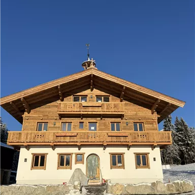 A cozy wooden house in alpine style, surrounded by snow. The clear blue sky gives the scene an inviting atmosphere.