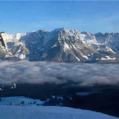 A winter landscape with snow-covered mountains and a cable car. In the background, there is a cloud blanket.