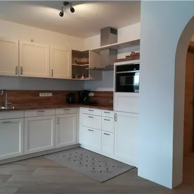 Eine moderne Küche mit weißenSchränken und Holzdetails. Sie ist gut ausgestattet und hat viel natürliches Licht.