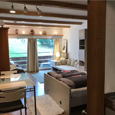 Ein gemütliches Zimmer mit einem Doppelbett, einem Sofa und einem großen Fenster. Der Raum hat Holzdetails und einen kleinen Esstisch.