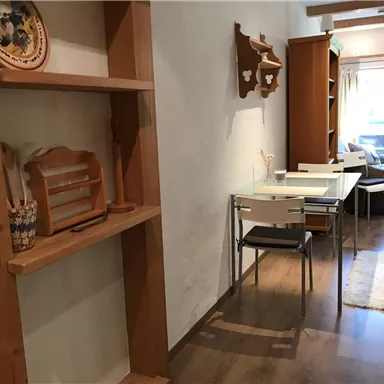 Ein heller Flur mit Holzregalen und einem Glastisch. Im Hintergrund sind Stühle und eine gemütliche Sitzecke sichtbar.