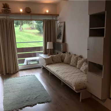 Ein gemütlicher Wohnraum mit einem hellen Sofa und einer Terrasse. Große Fenster lassen viel Tageslicht herein und bieten einen Blick ins Grüne.