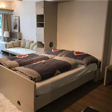 Ein gemütliches Schlafzimmer mit einem Bett und einer modernen Sitzecke. Große Fenster lassen viel Licht herein und geben einen Blick auf die Natur.