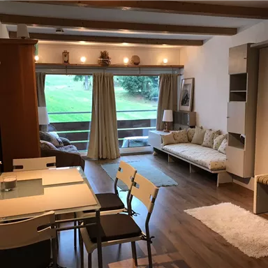 Ein gemütliches Wohnzimmer mit einem Esstisch und Stühlen. Große Fenster bieten einen Blick auf die grüne Landschaft.