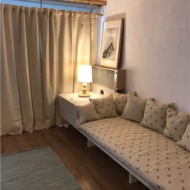 Ein gemütlicher Wohnraum mit einem gepolsterten Sofa und einer Stehlampe. Vorhänge und ein Teppich ergänzen das einladende Ambiente.