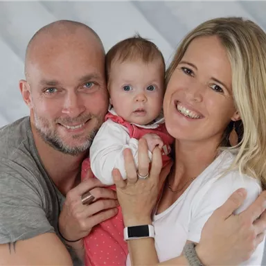 Eine glückliche Familie mit einem Baby. Der Vater und die Mutter umarmen ihr Kind und lächeln.