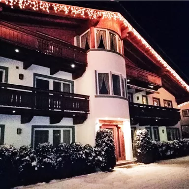 Ein gemütliches Chalet mit Weihnachtsbeleuchtung bei Nacht. Der Schnee umgibt das Gebäude und schafft eine festliche Atmosphäre.